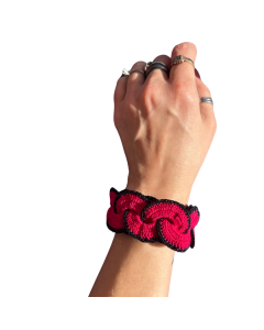 Artisan crochet bracelet in pink and black displayed on a hand with rings, showcasing handmade detail.